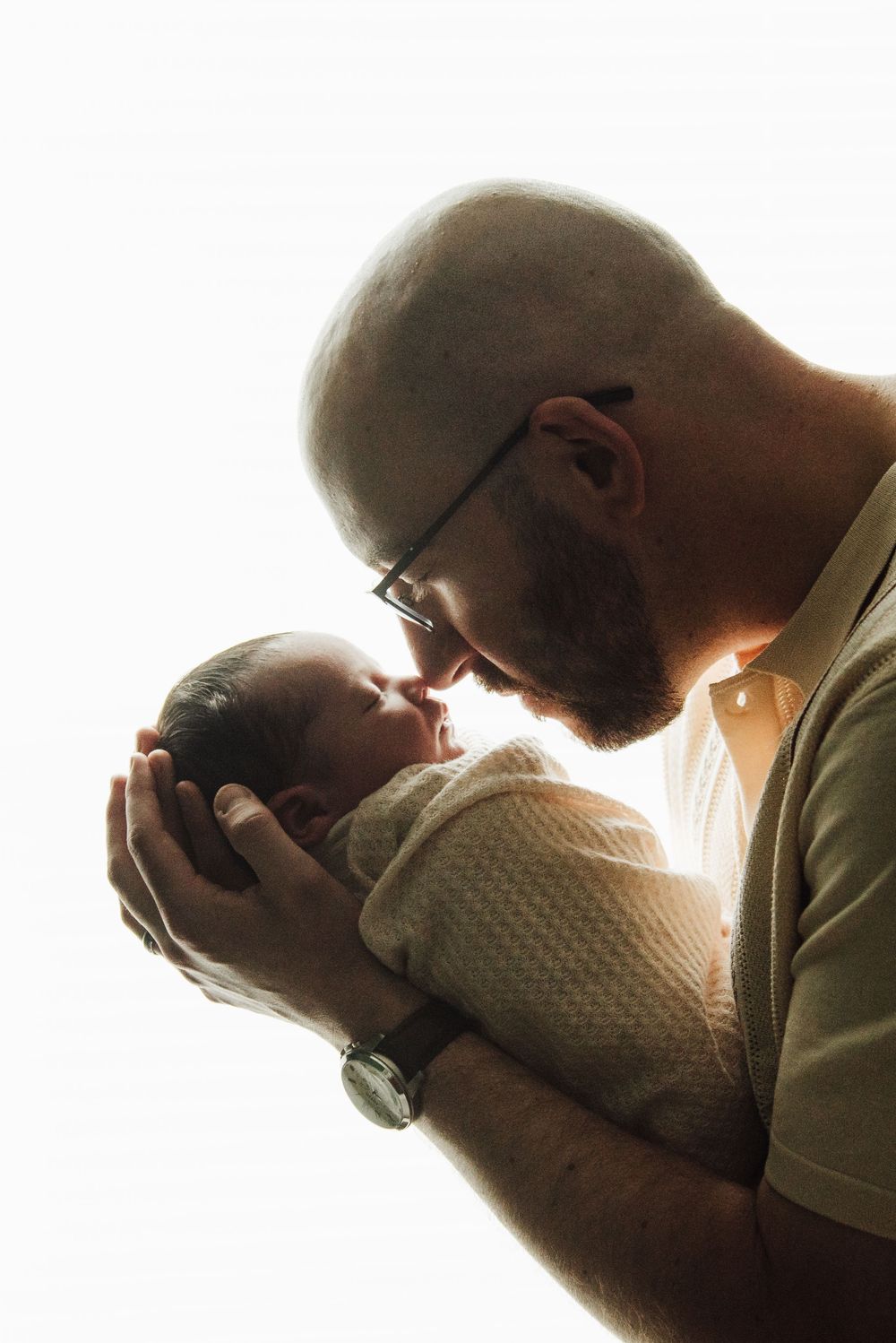 A tender silhouette of a parent and baby sharing an intimate moment in warm backlit glow.