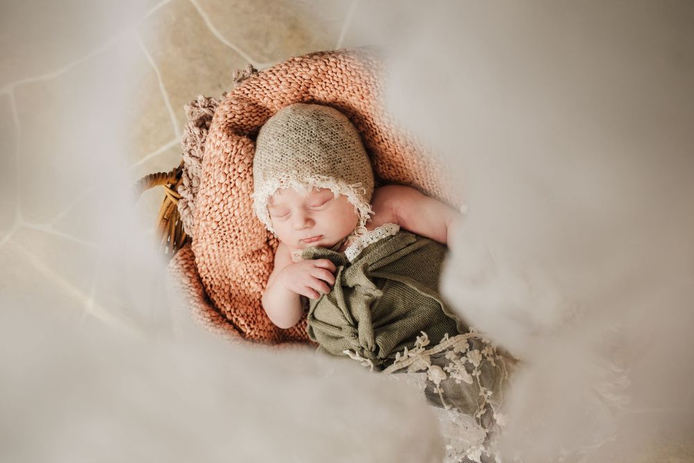 Newborn baby wrapped in soft neutral-toned blankets lying on textured backdrop in professional studio setting.