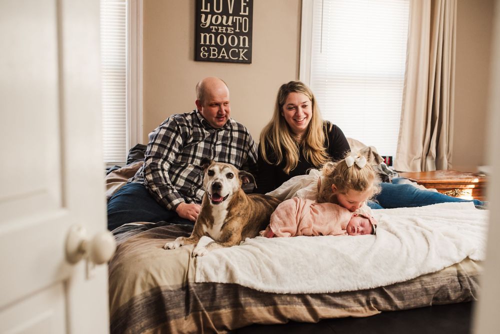A family relaxes on a bed with their dog while spending quality time together in a cozy bedroom.
