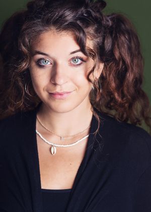 A series of close-up portraits in dark lighting shows someone with curly brown hair wearing a black blazer and pearl necklace.