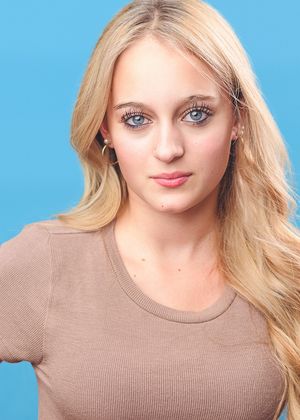 Blonde model in beige sweater poses for headshots against bright blue background.
