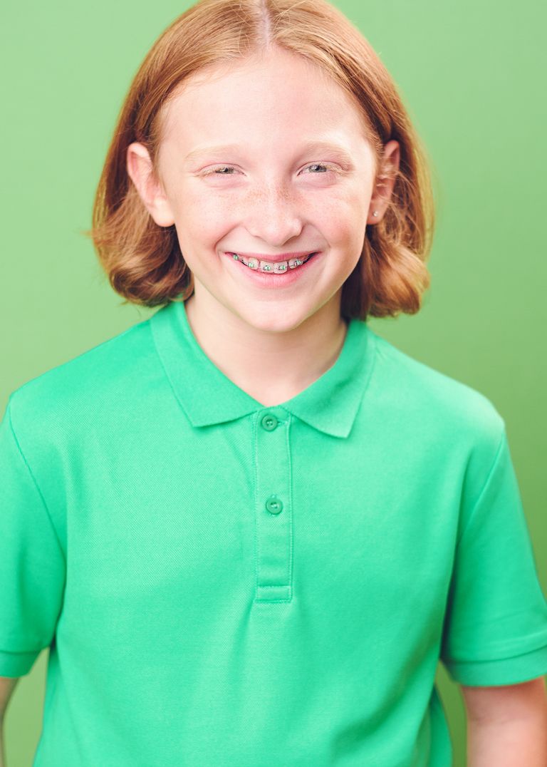 A person wearing a bright green polo shirt smiles warmly against a mint green background.