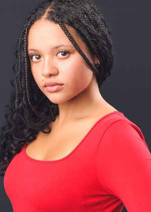 Professional portrait of a woman with braided hair wearing a red top against a dark background.