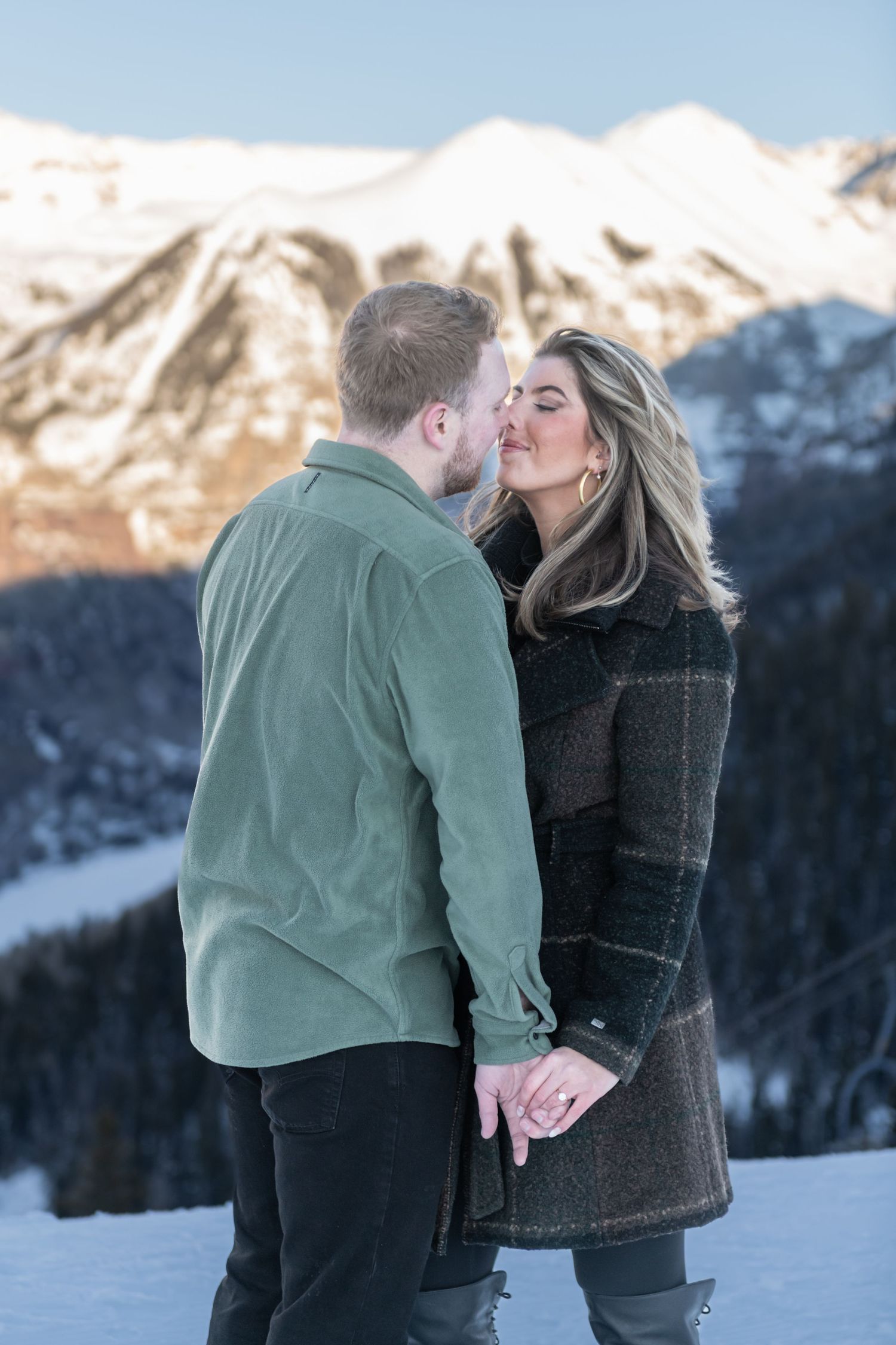 A newly engaged couple shares a tender kiss against a snowy mountain backdrop in winter near Telluride.