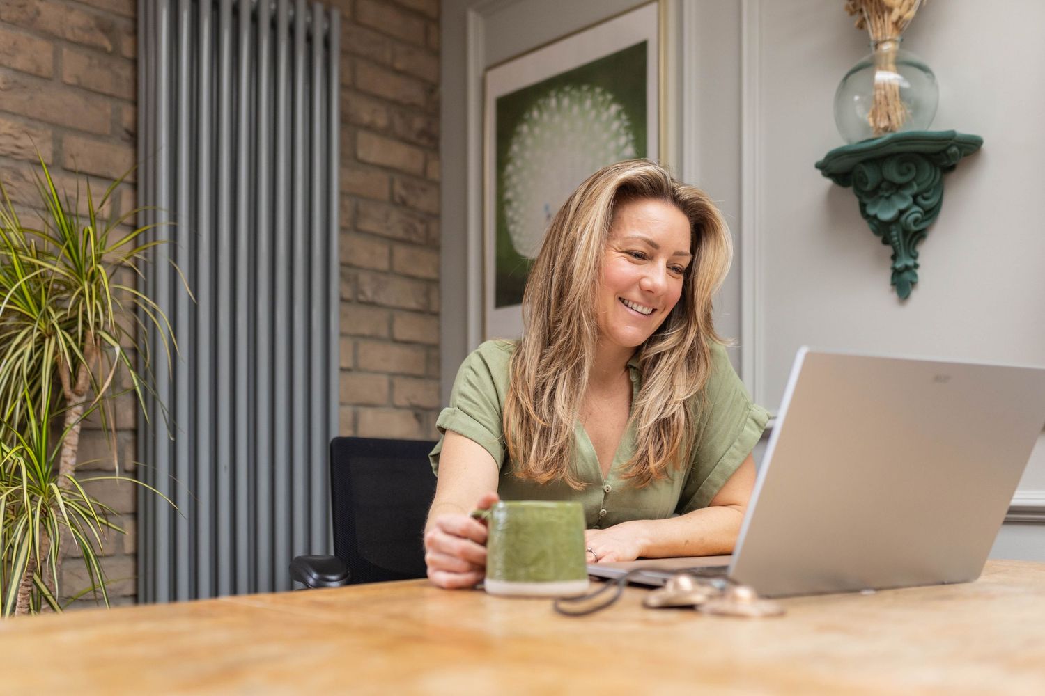 woman sits at a table with her lap top open and a cup of tea. she is a therapist having her photo taken for her personal brand shoot