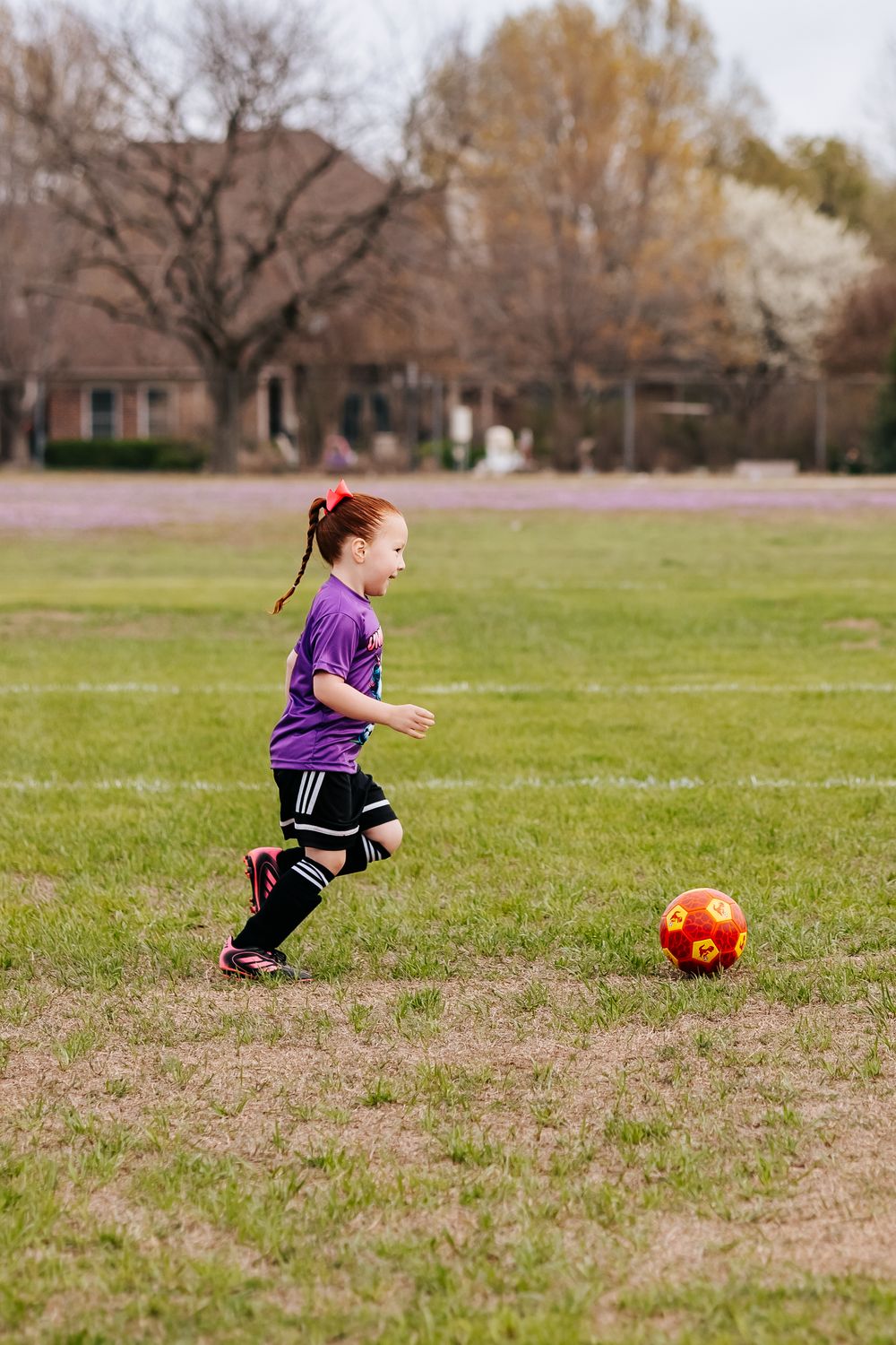 Sequence of child in purple outfit running to kick orange ball in grassy field.