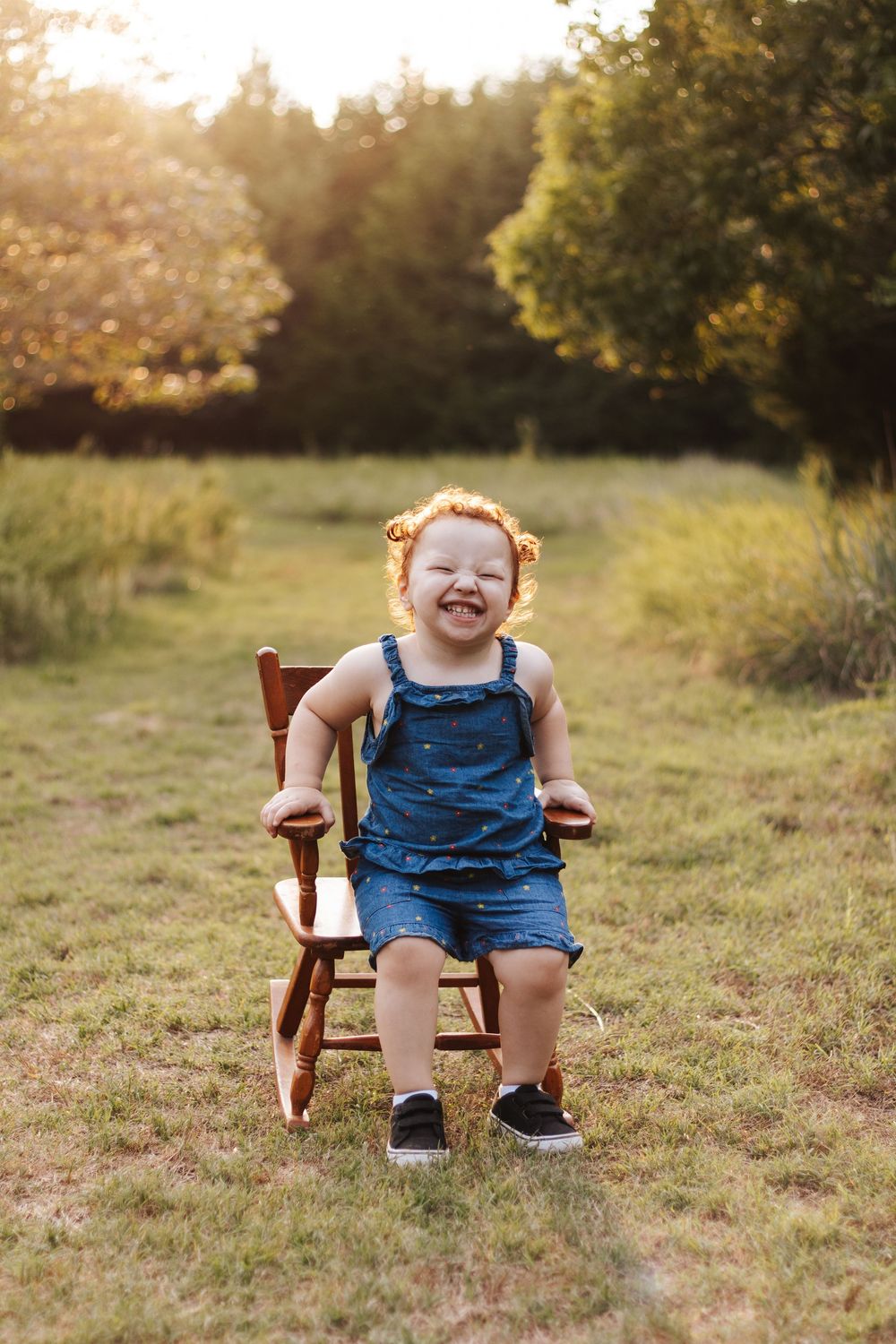 Child sitting in wooden chair outdoors during golden hour photoshoot.