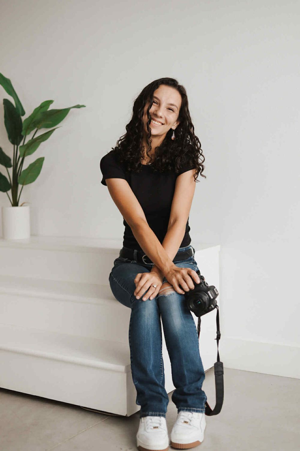 A casual photographer sits relaxed on a white bench with camera in hand.