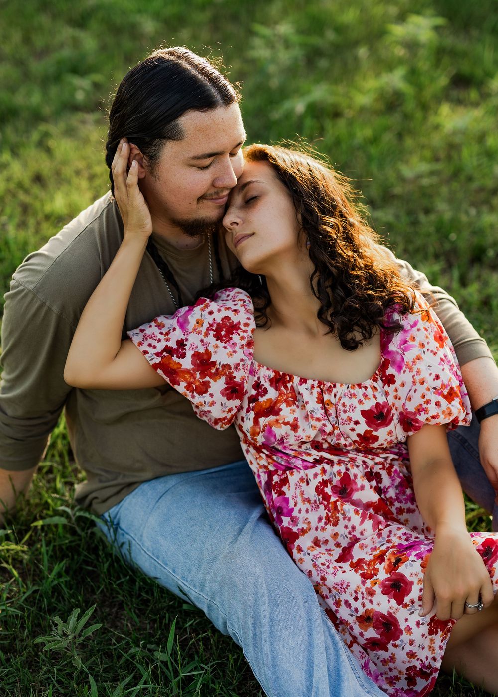 A couple shares a romantic moment while sitting in lush green grass.