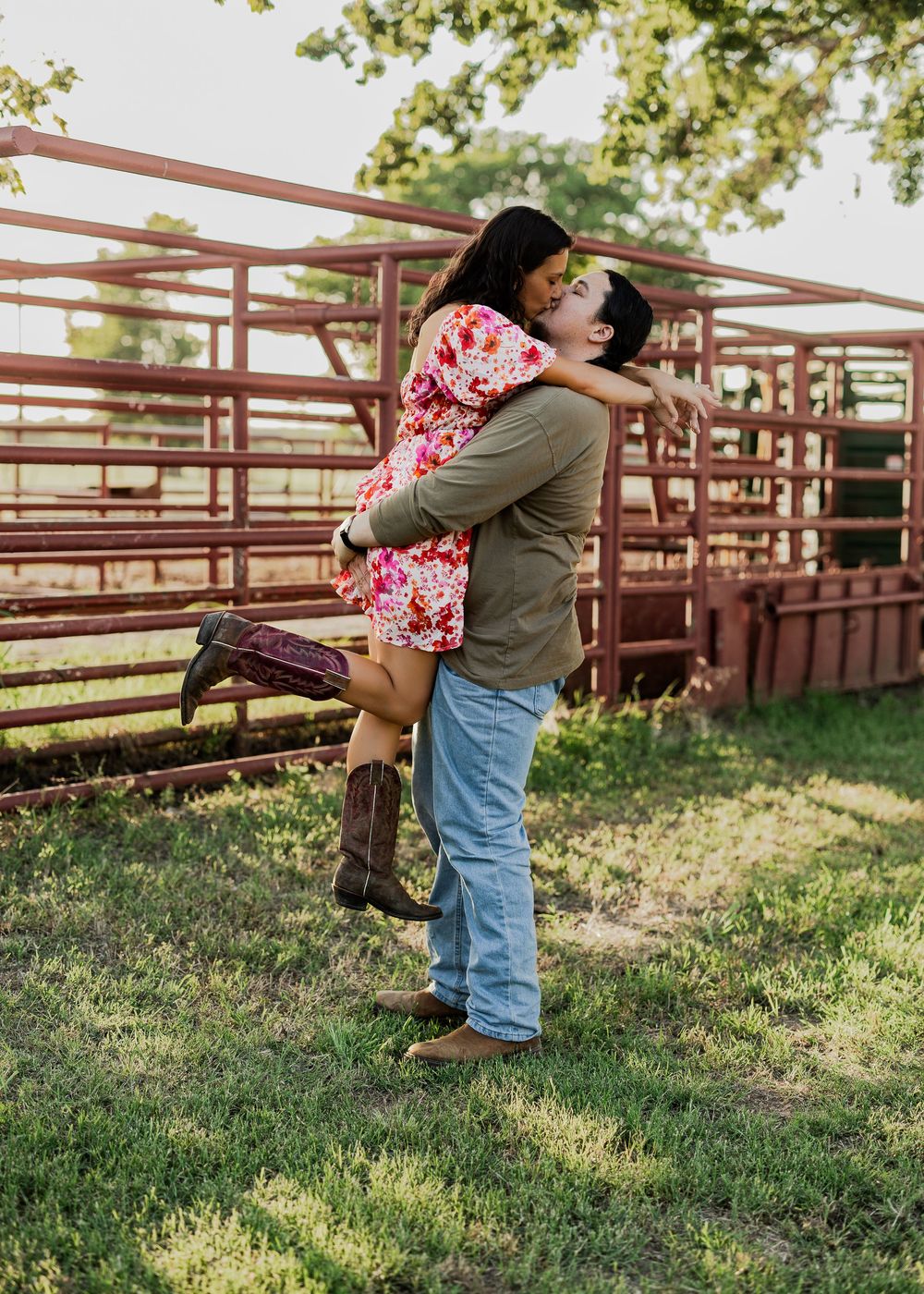Romantic couple embracing in a rustic farm setting with wooden fencing at sunset.