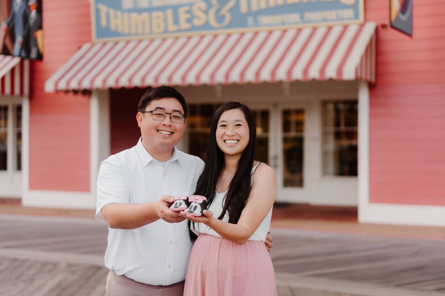 A couple poses together in front of a pink building with striped awnings and brick walls.