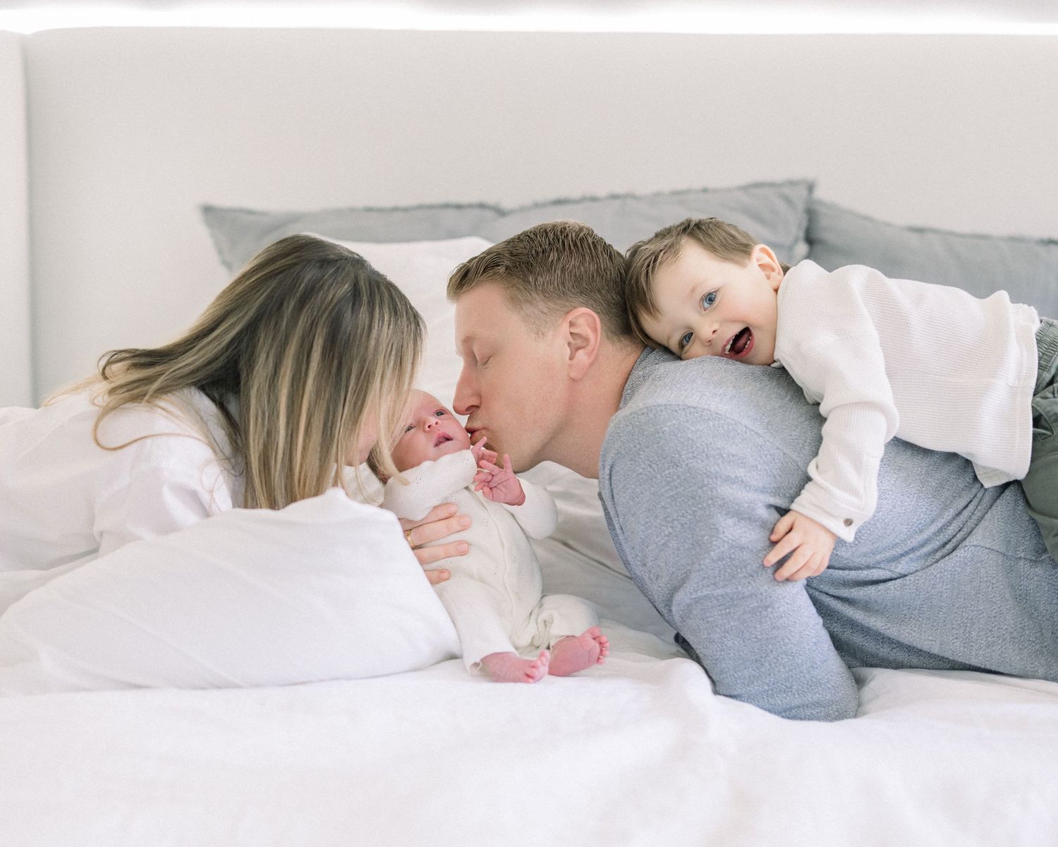 A couple lying together on white bedding shares an intimate moment while dressed in casual clothing.