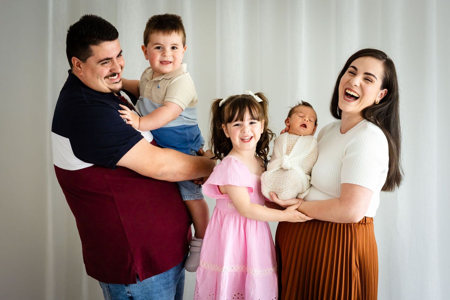 Happy family of five posing for a portrait, parents holding three young children including a newborn baby.
