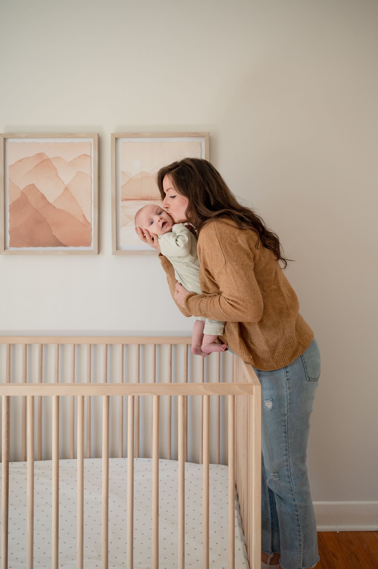 A happy baby wearing a cream sweater lies on a brown blanket while being tickled and laughing joyfully.