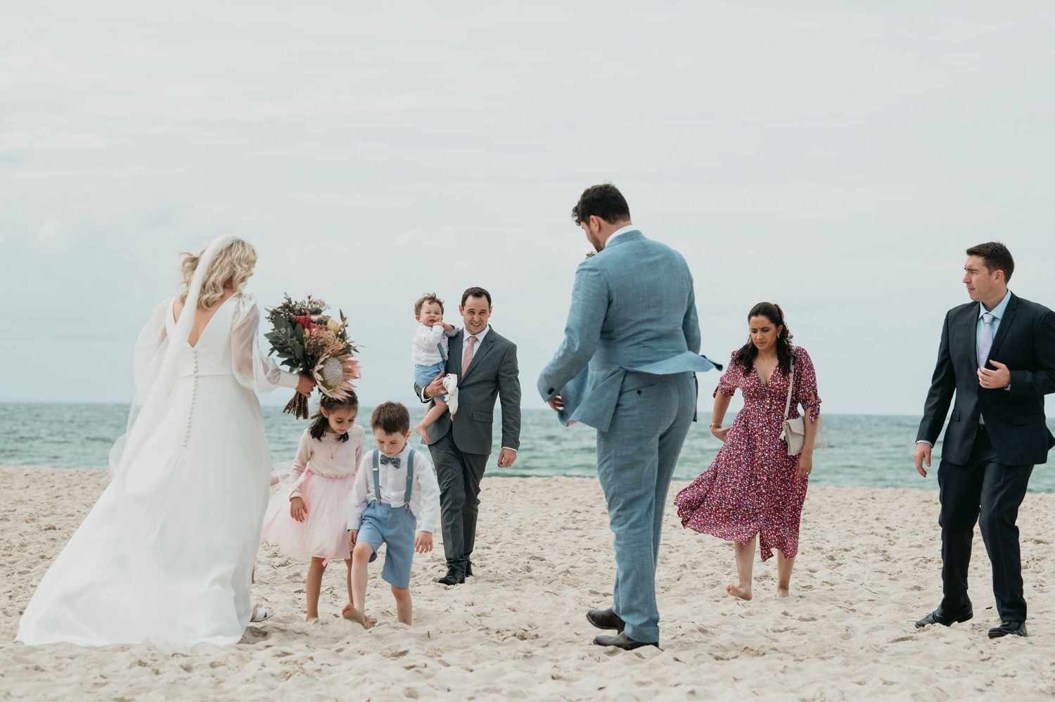 A stunning destination beachfront wedding party enjoying a beautiful sunset celebration together on a sandy shore.