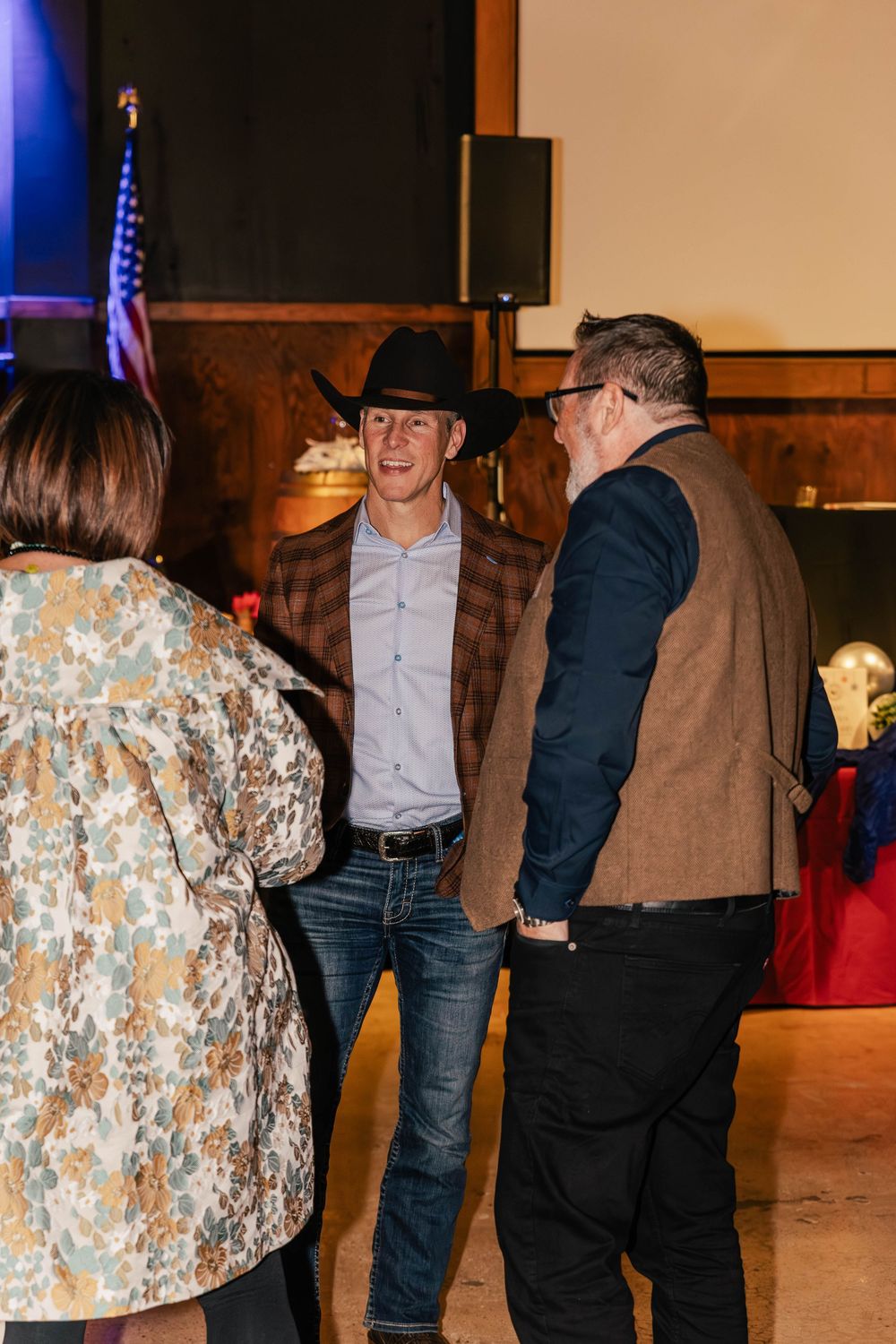 Event attendees in western attire socializing in front of an American flag backdrop.