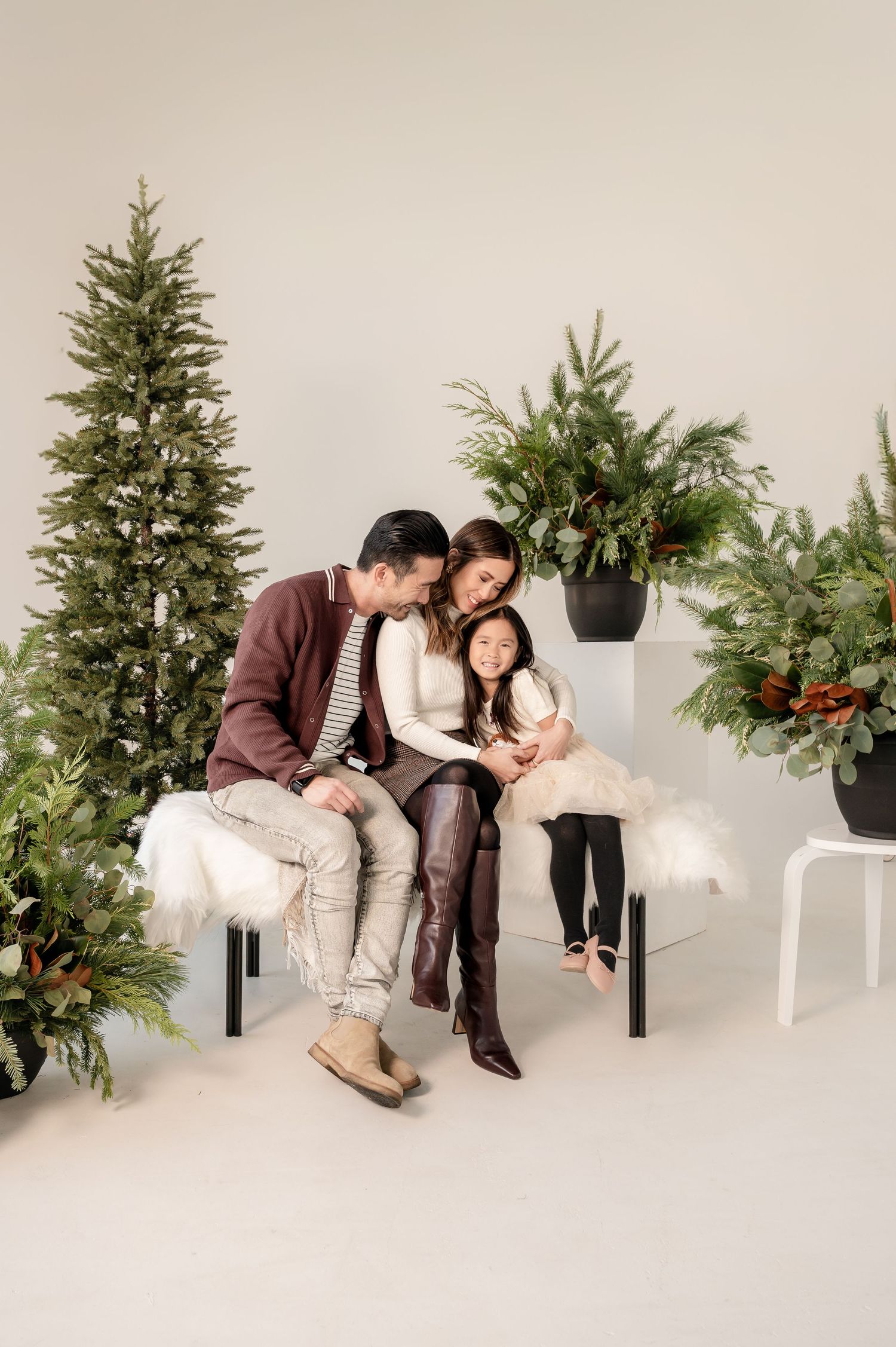 A couple poses together on a white couch with holiday greenery and a Christmas tree in the background.