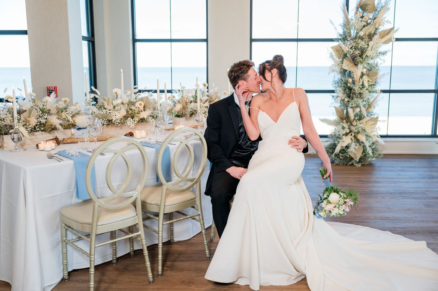 A wedding reception setup in a bright venue with white linens, floral arrangements and elegant table settings.