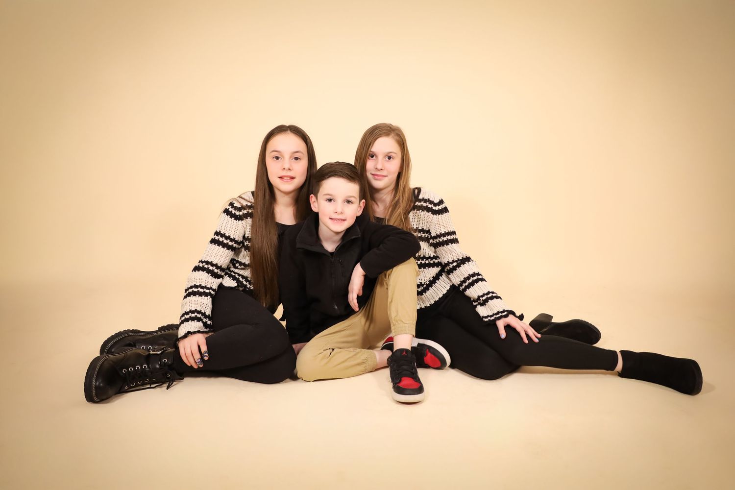 Friends posing playfully on beige backdrop in casual black and striped outfits.