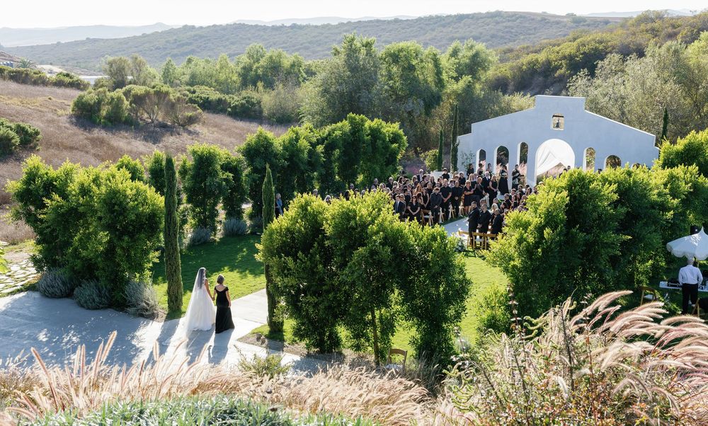 Panoramic view of a hillside wedding venue with white buildings and cypress trees.