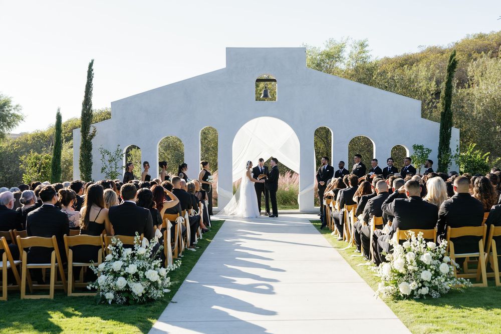 White wedding ceremony venue with wooden chairs and floral arrangements overlooking a scenic landscape.