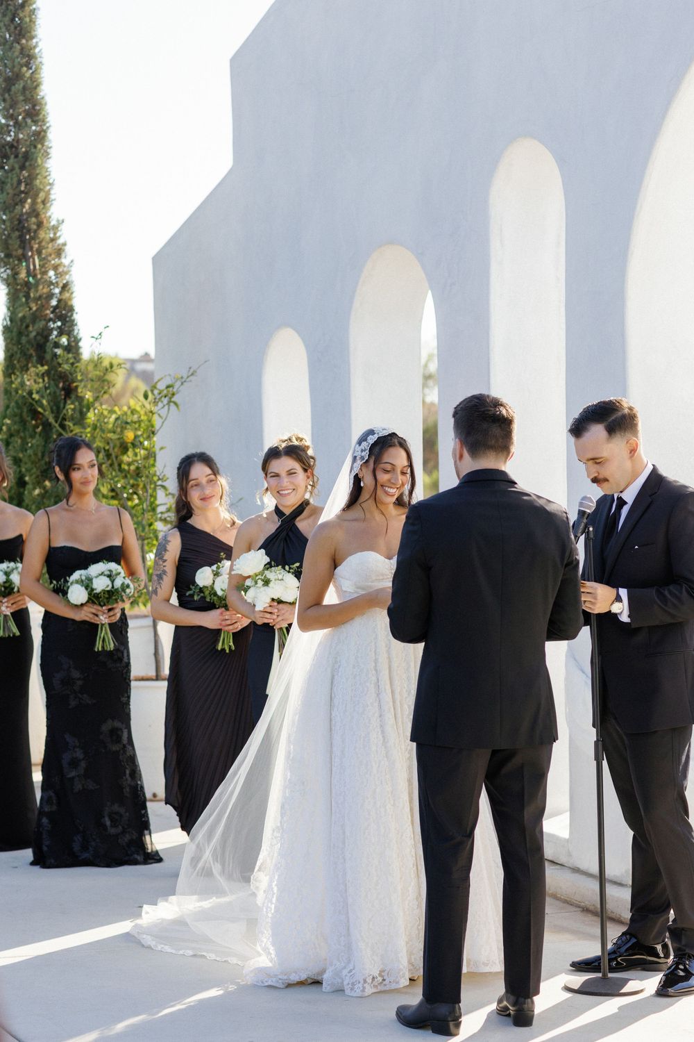 Wedding party lined up against white archways during an outdoor ceremony.