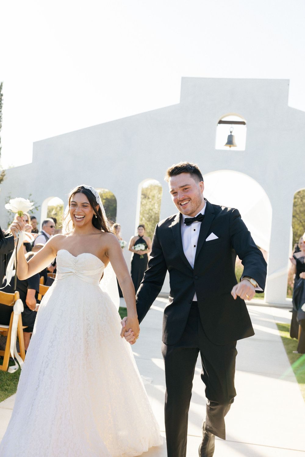 Joyful moments captured at an outdoor wedding ceremony with white architectural backdrop.