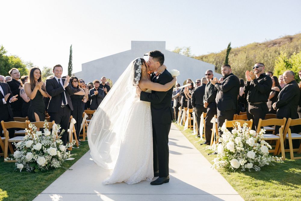 Wedding ceremony in progress with guests seated outdoors against a scenic mountain backdrop.