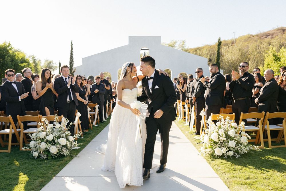 Wedding ceremony setup with white chairs and floral arrangements against mountain backdrop at sunset.