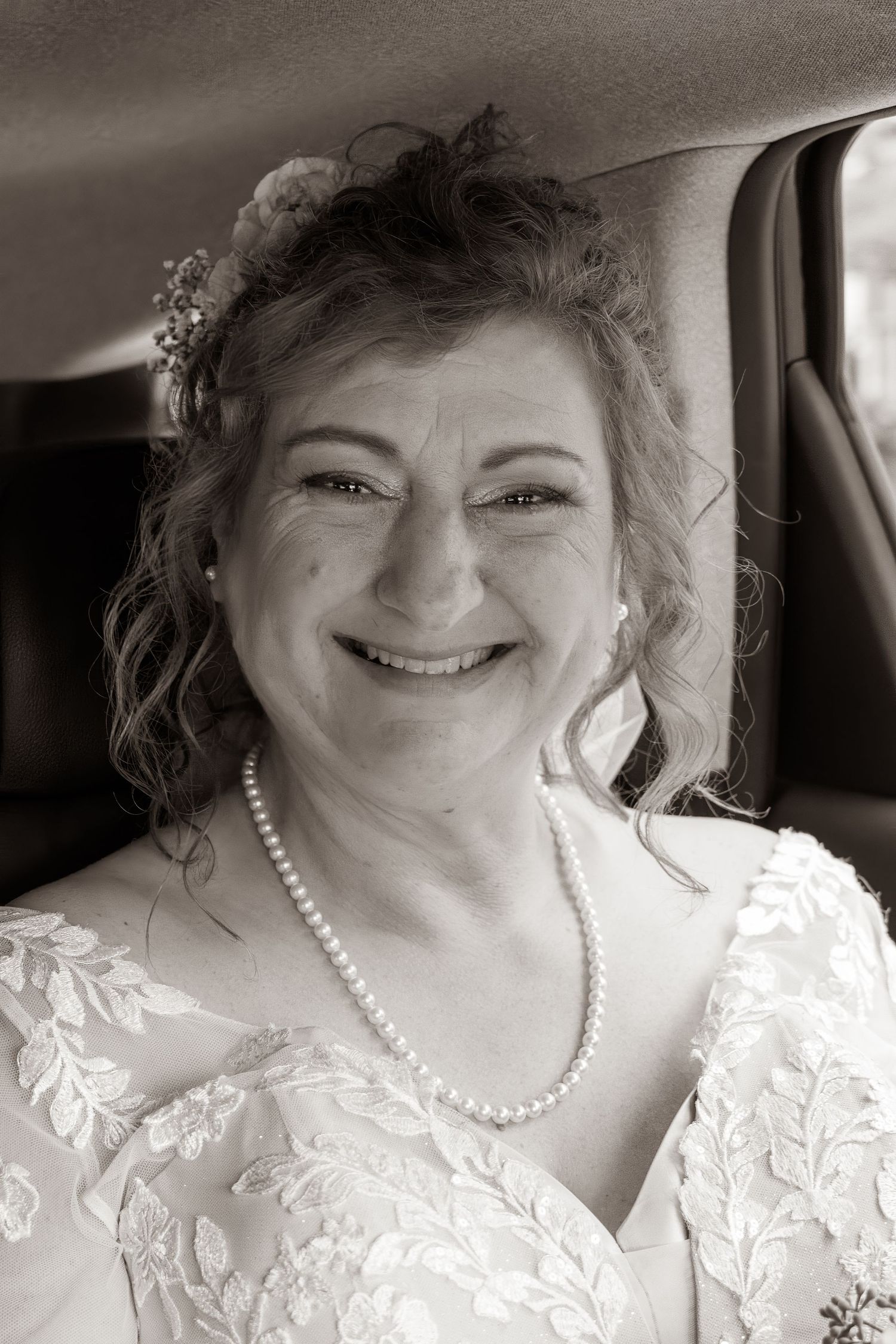 Frederick Maryland Wedding Photographer   A person wearing a white lace dress and pearl necklace smiles in a car.
