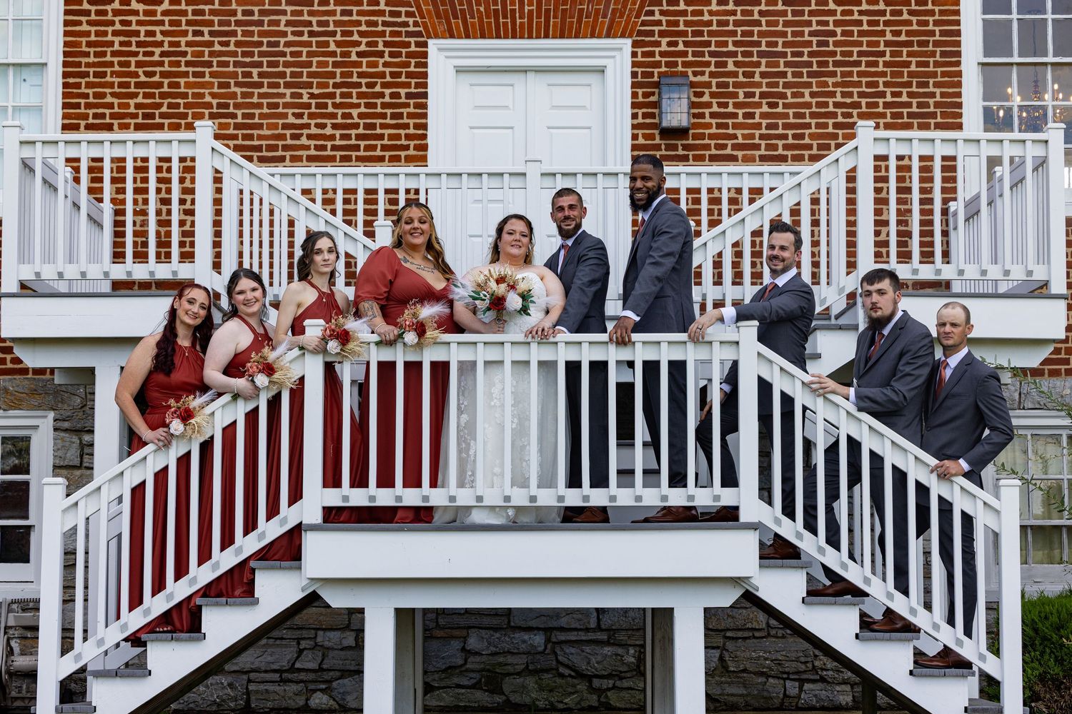 frederick maryland wedding photographer Wedding party members posing on white stairs and railings of a classic brick building.