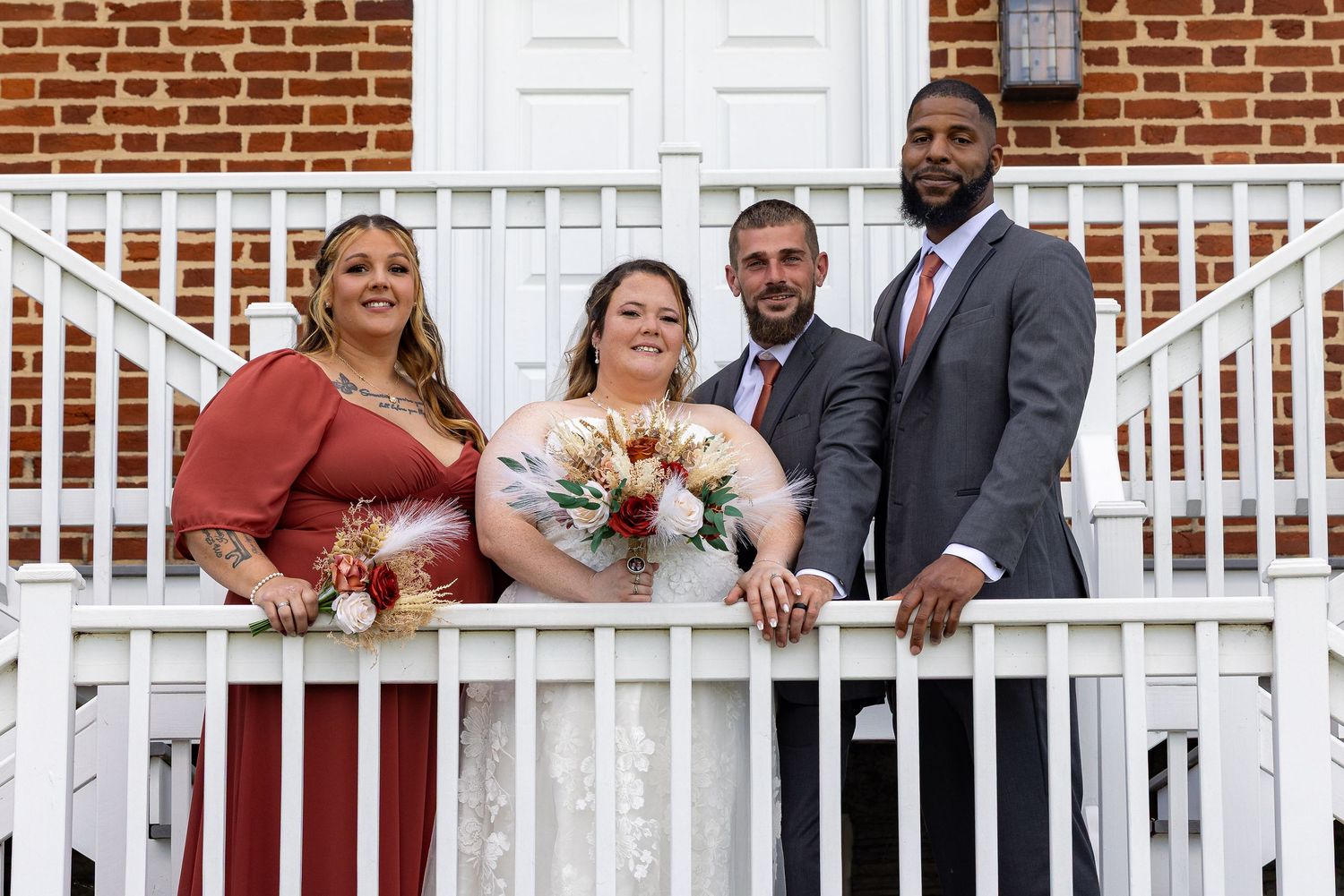 frederick maryland wedding photographer Wedding party members lined up on a white porch railing against a brick building backdrop.