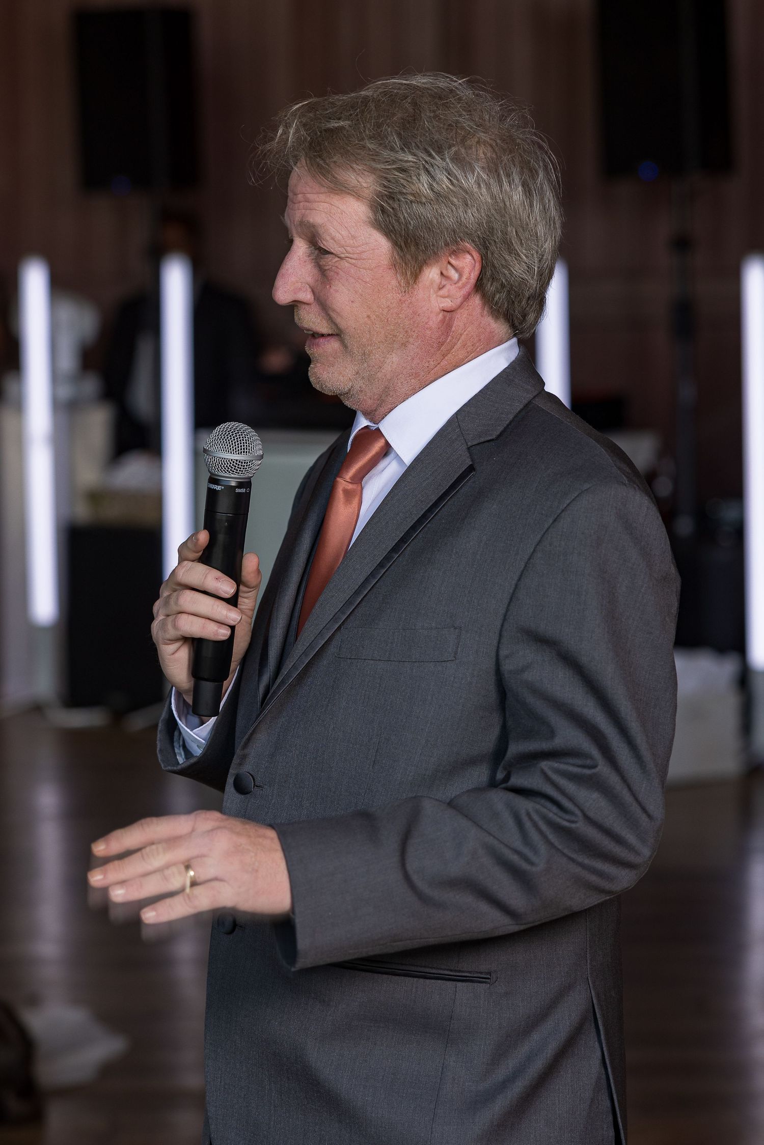 frederick maryland wedding photographer Speaker in a dark suit delivering a speech at an indoor wedding reception.