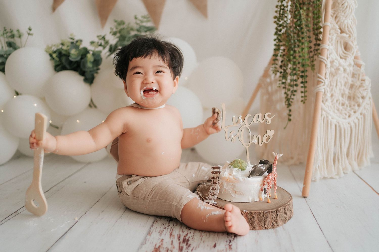 A baby sits on a white blanket during a first birthday cake smash photo session with rustic decorations.