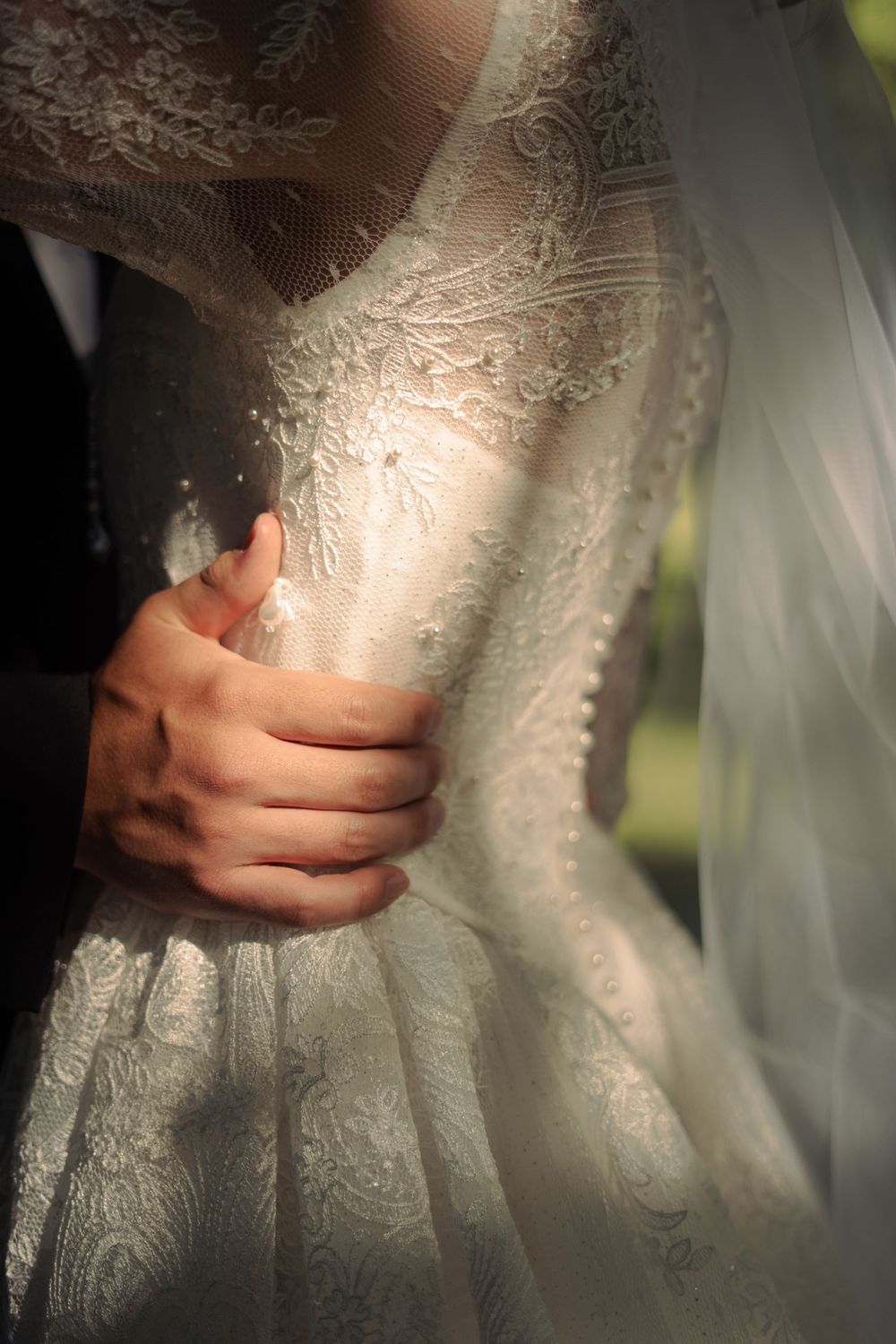 Close-up of groom's hand tenderly holding bride's lace wedding dress waist.