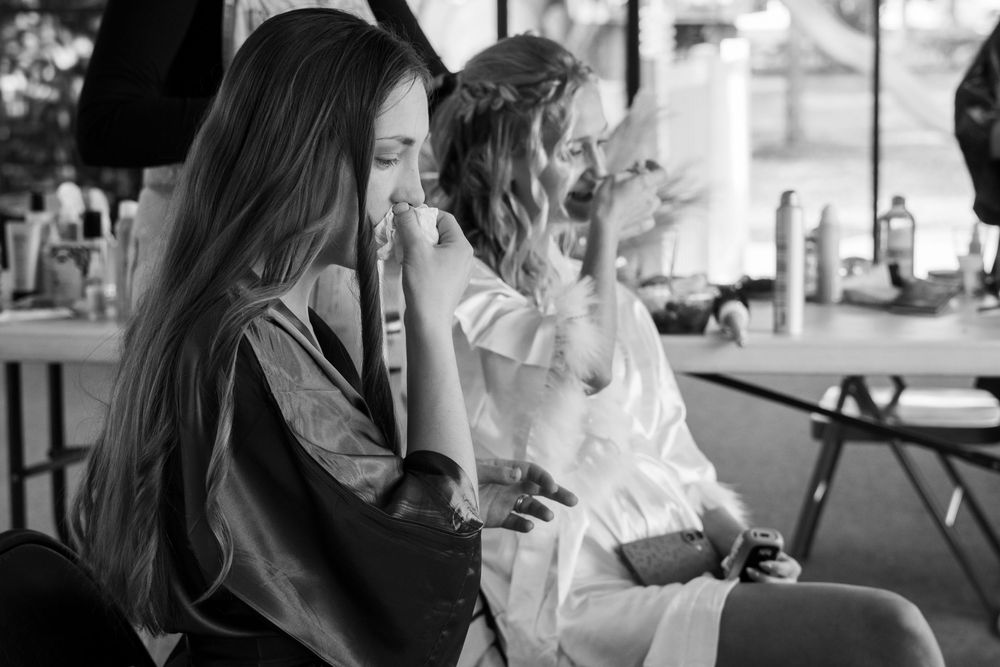 Black and white candid photo of two women laughing together during wedding preparations indoors.