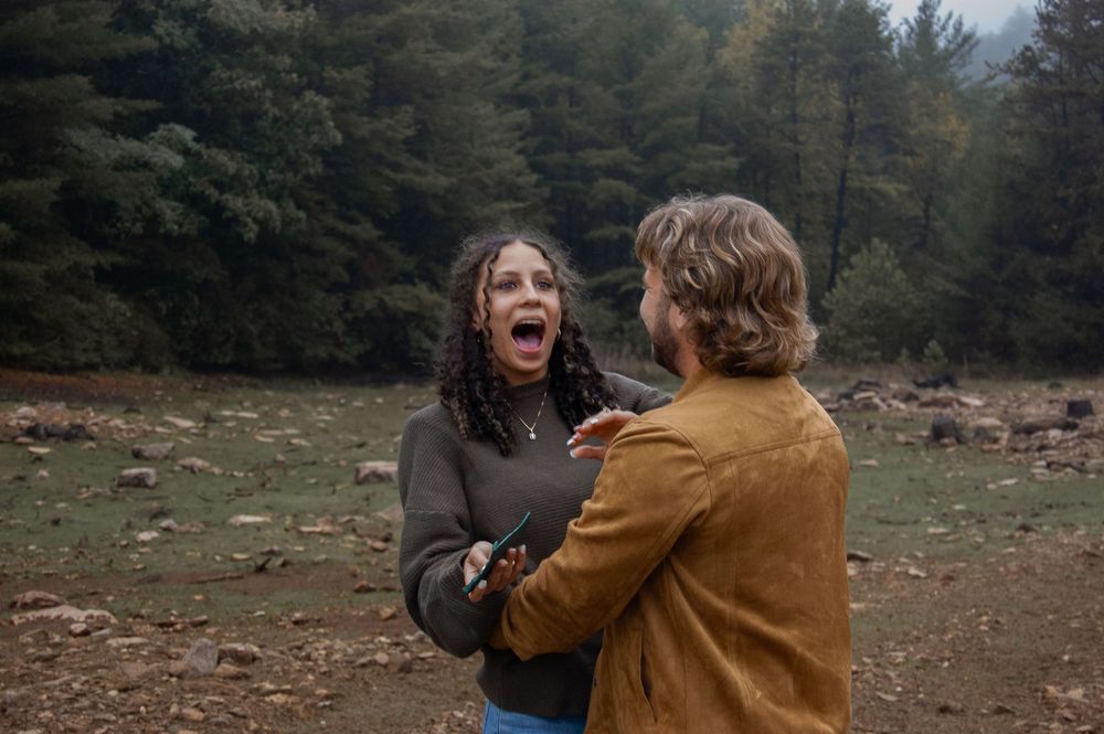 Couple having an emotional outdoor argument in a misty forest clearing, woman screaming with mouth open wide.