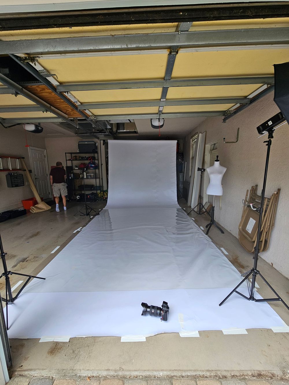 A photography studio setup showing a white seamless backdrop and lighting equipment mounted on the ceiling.