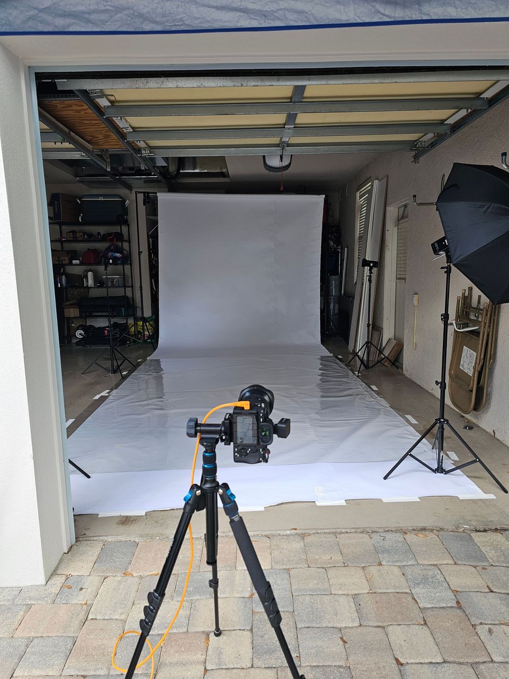 Professional photography studio setup with multiple tripods and seamless white backdrop in a garage space.