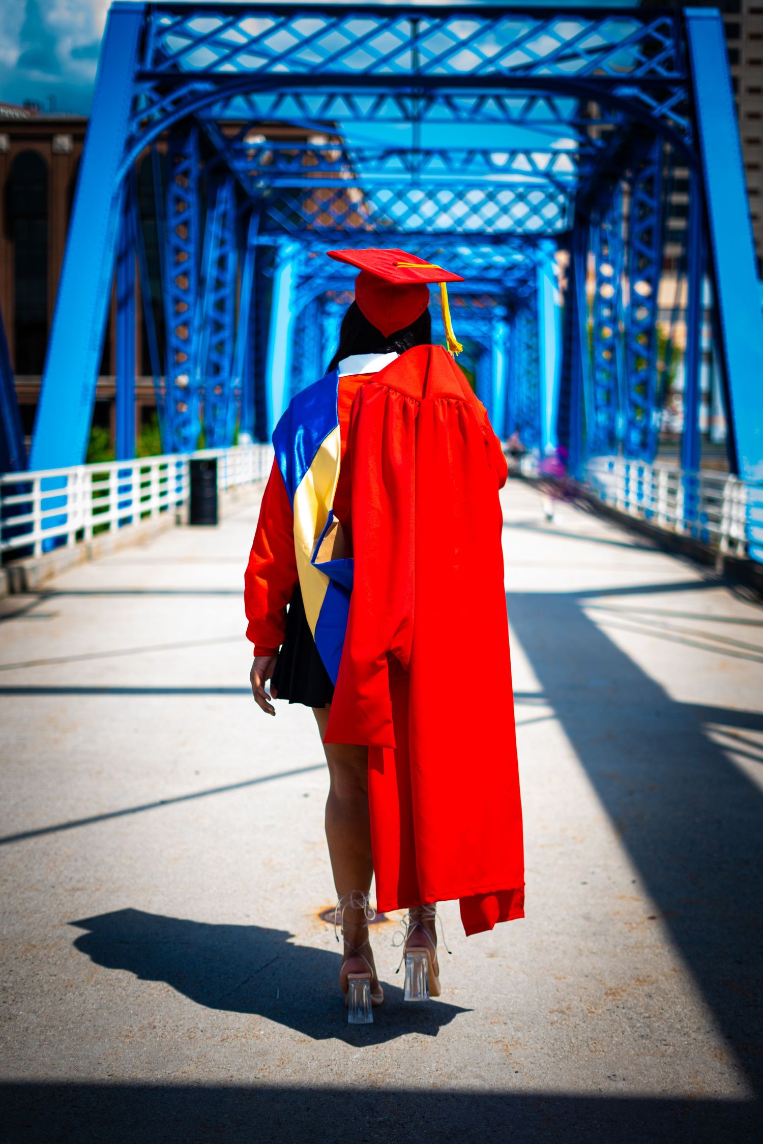 Red graduation gown silhouette walking across blue-painted bridge structure.
