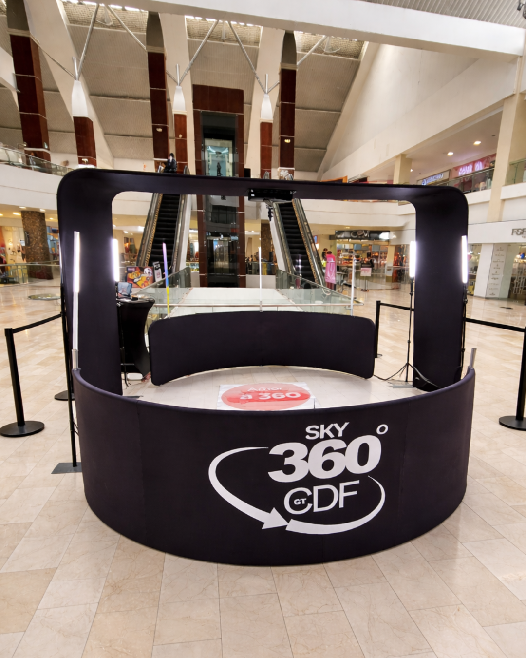 A circular black promotional kiosk for Sky 360 CDF with LED lighting stands in an empty shopping mall atrium.