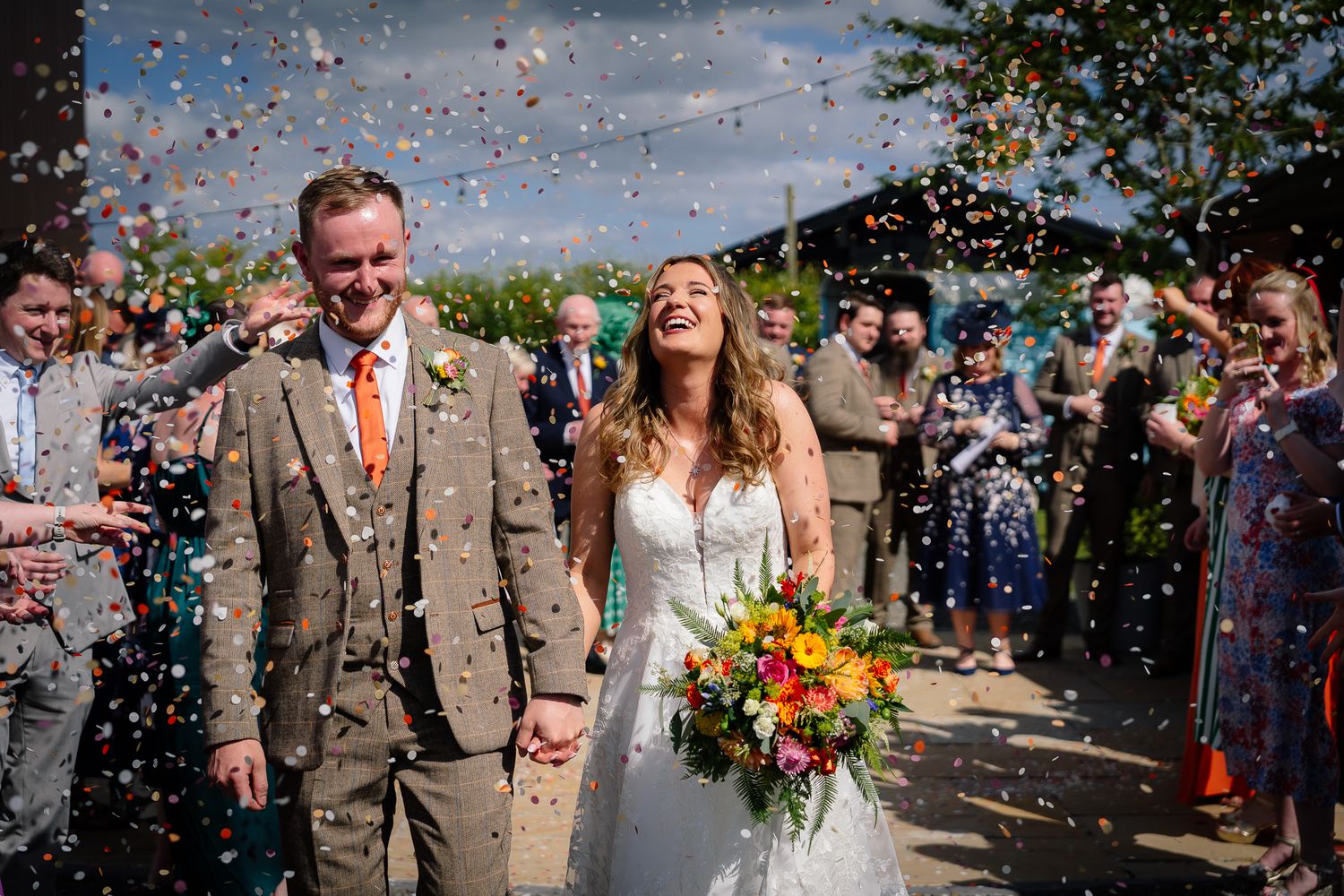 Wedding guests shower the newlyweds with colorful confetti during an outdoor celebration.