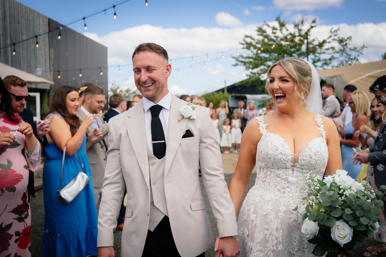 Wedding guests dance and celebrate on an outdoor patio decorated with string lights during a lively reception party.