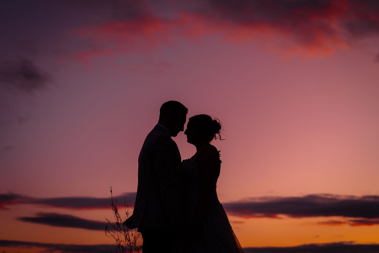 Silhouette of a couple embracing against a dramatic pink and purple sunset sky.