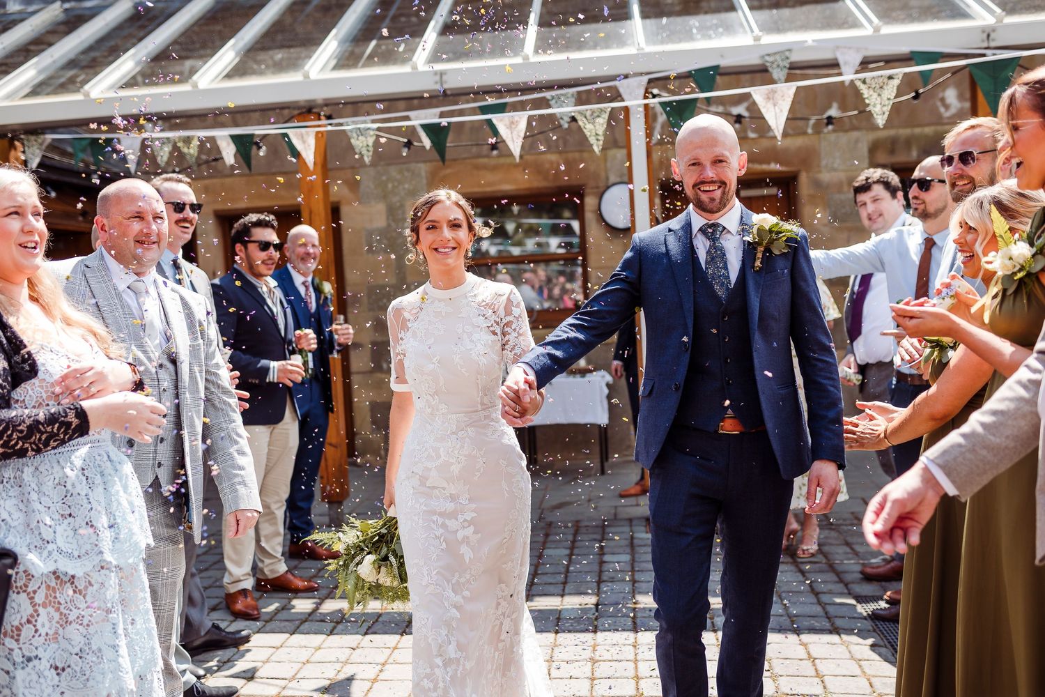 Wedding guests celebrate and dance under decorative bunting at an indoor reception venue.
