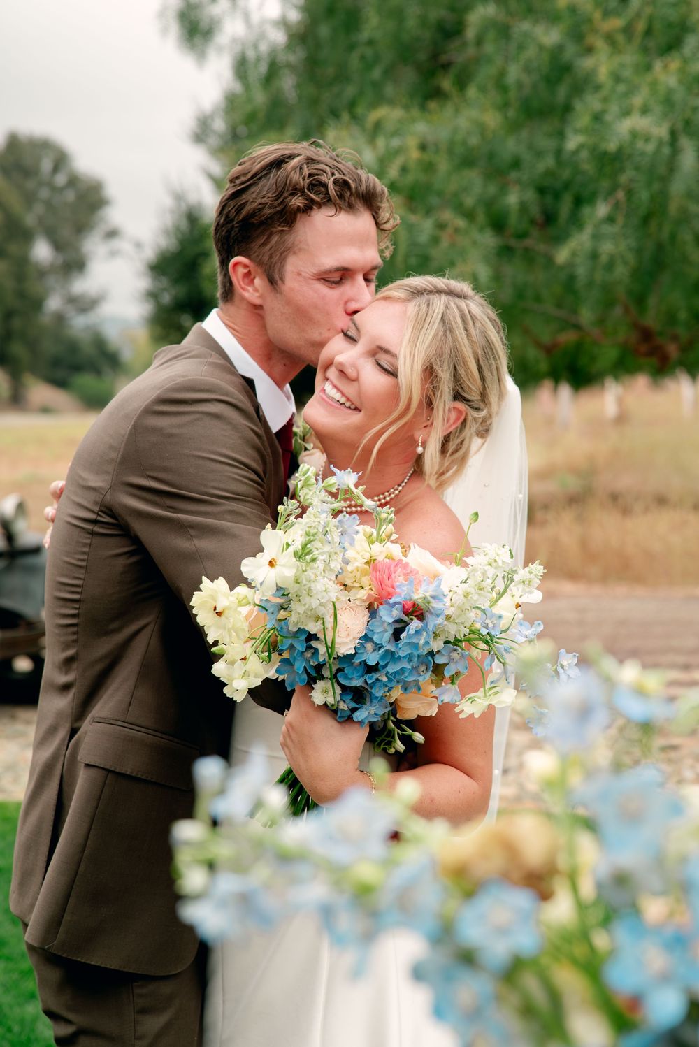 A romantic outdoor wedding scene with delicate blue flowers in the foreground and a natural field setting.