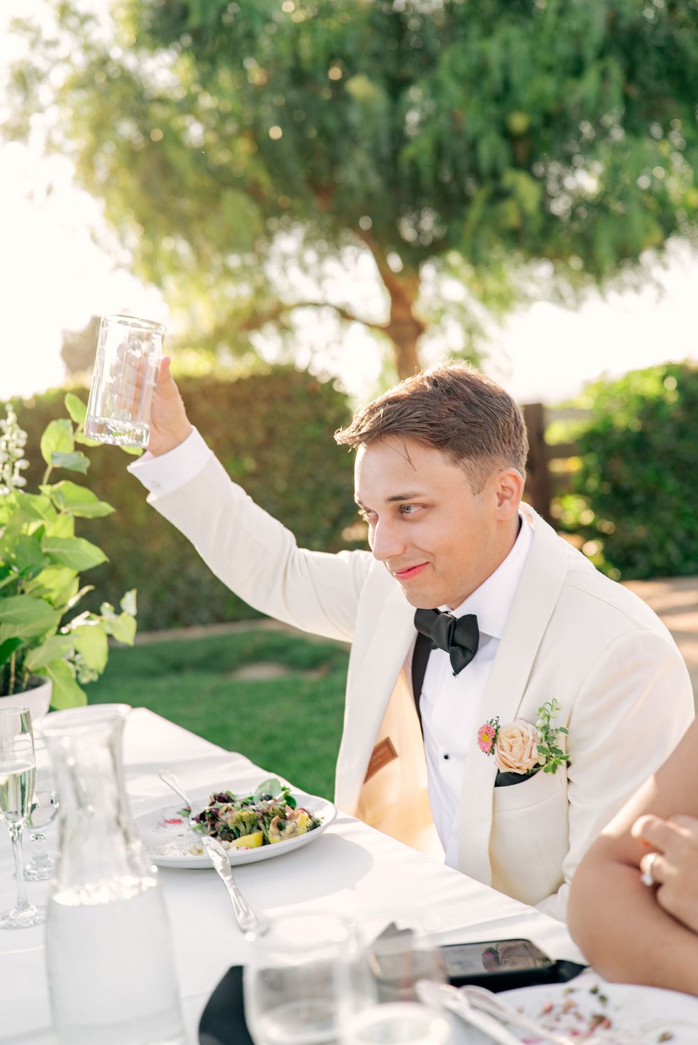 Wedding guests raise champagne glasses in a toast at an elegant outdoor reception during golden hour.