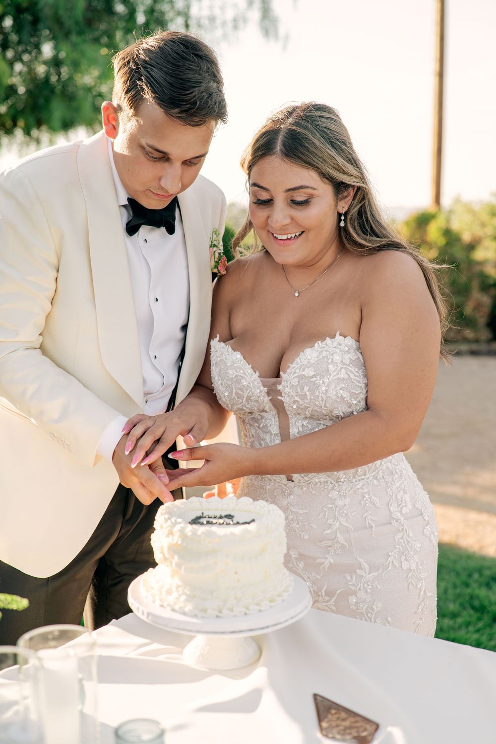 A couple in wedding attire share a sweet moment while cutting their white wedding cake together.