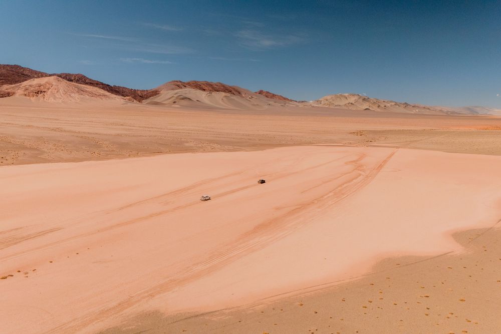 Desert landscape with rolling sand dunes and distant mountains under bright blue sky in arid terrain.