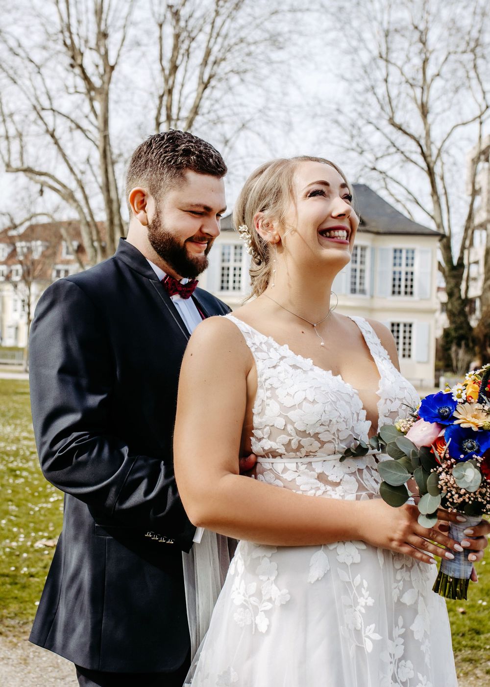 A joyful couple shares laughter and embraces during their outdoor wedding celebration in a natural setting.